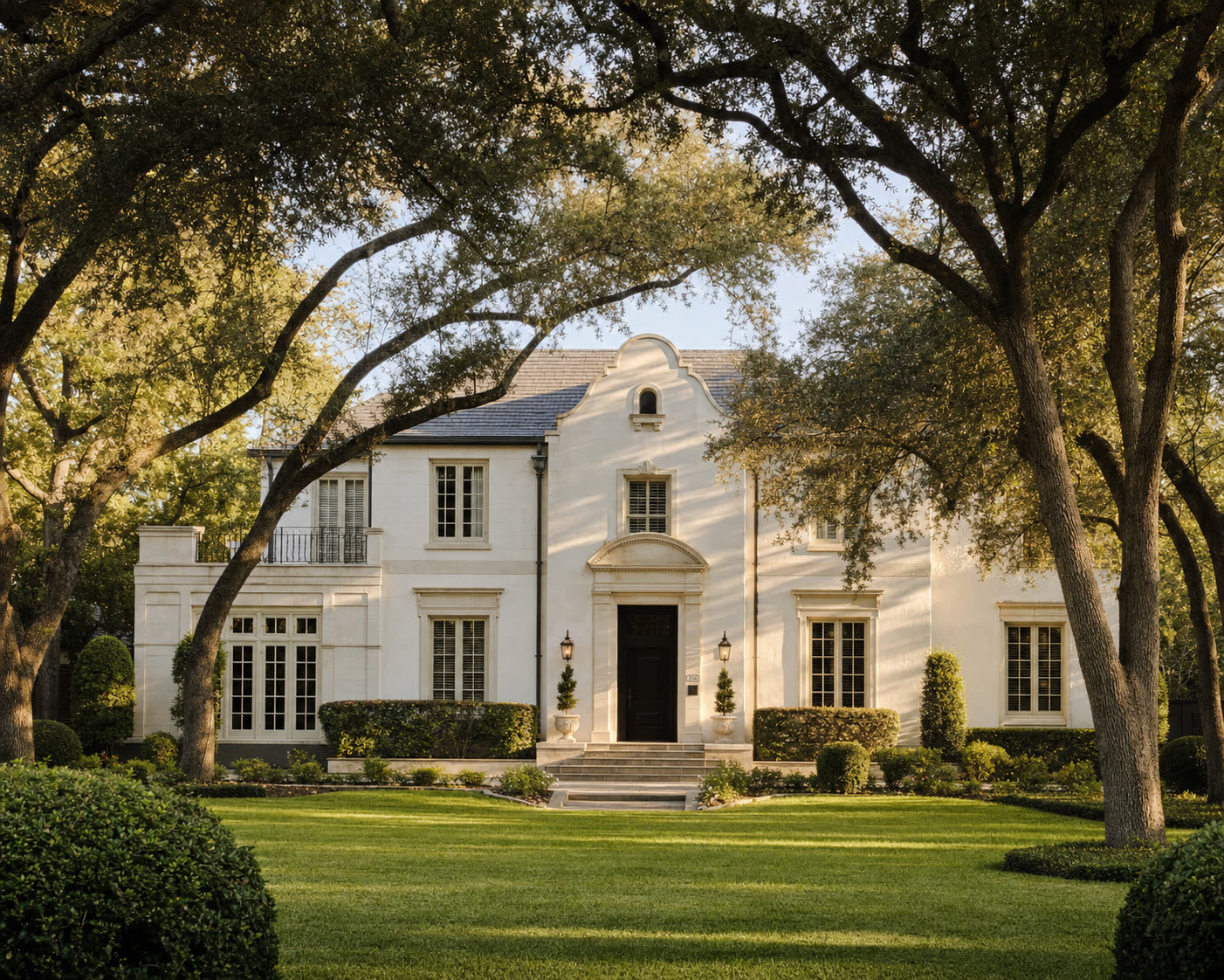 A stately white limestone estate home framed by live oak trees in an established San Antonio neighborhood